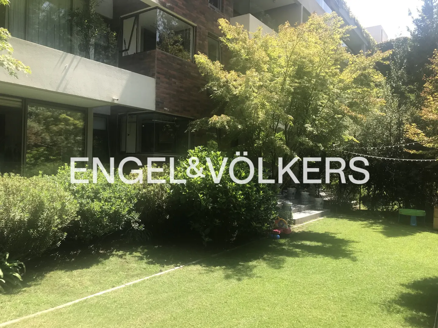 A modern building with a green lawn and trees. The Engel & Völkers logo is superimposed on the image.