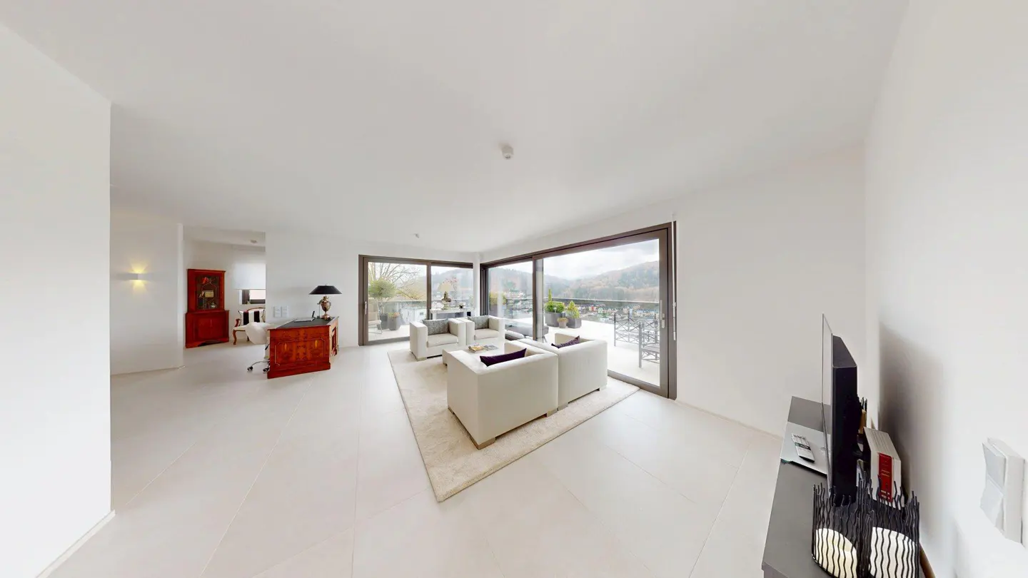 Bright, modern living room with white walls, tile floor, and furniture. Large windows overlook a balcony and scenic landscape.