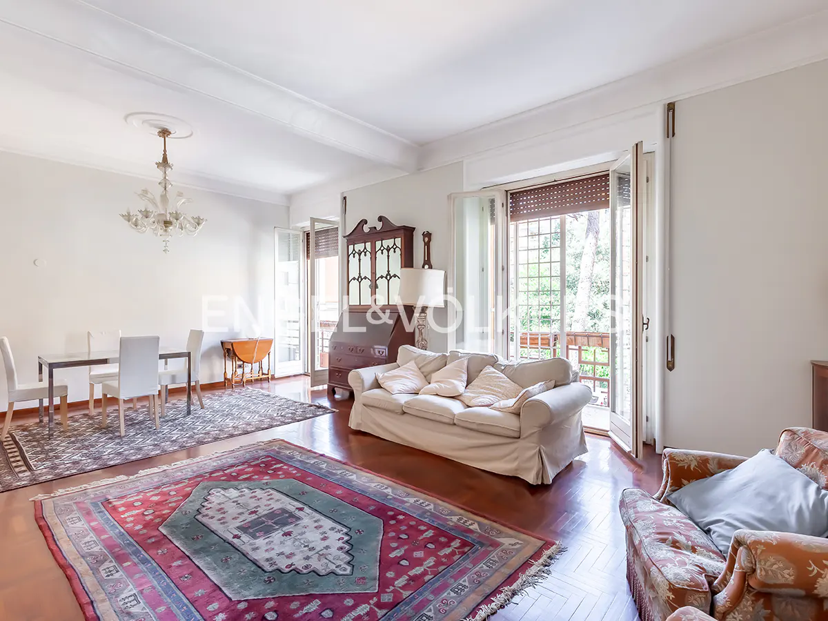 Bright living room with a white sofa, patterned rugs, dining area, and glass doors opening to a balcony.