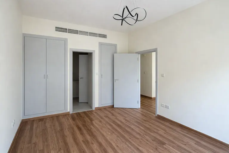 Empty room with wood floors, white walls, and gray trim. Two doors and a closet are visible. A modern light fixture hangs from the ceiling.