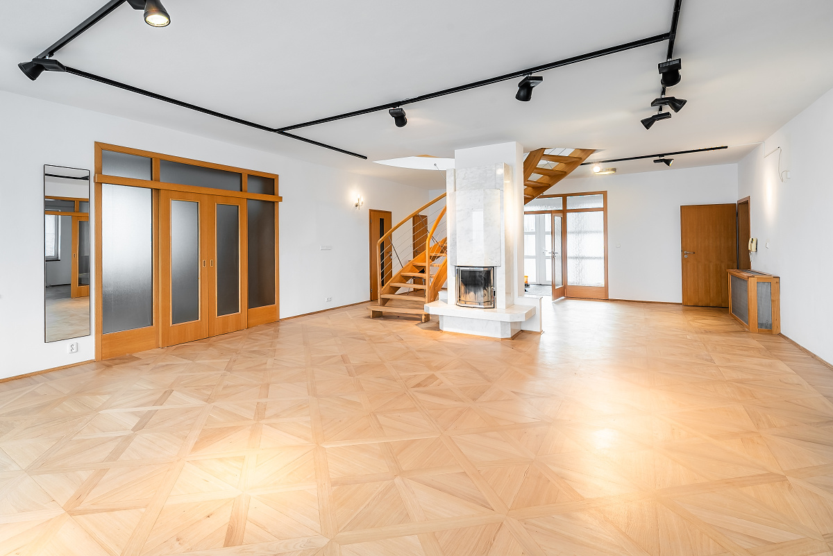 Spacious living room with light wood parquet flooring, a central fireplace, and a wooden staircase under track lighting.