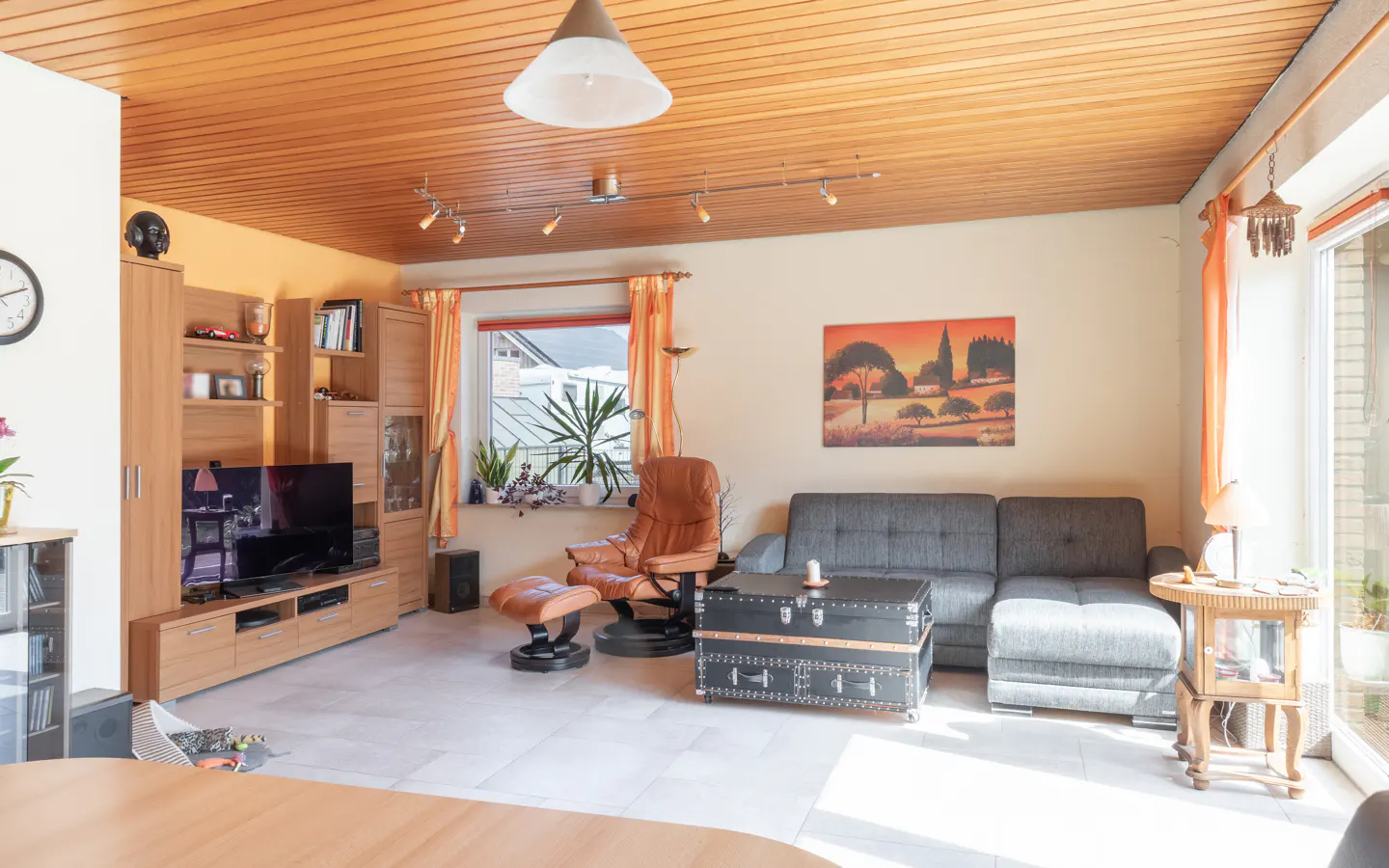 A living room with wood-paneled ceiling, gray sofa, leather chair, and a trunk-style coffee table.