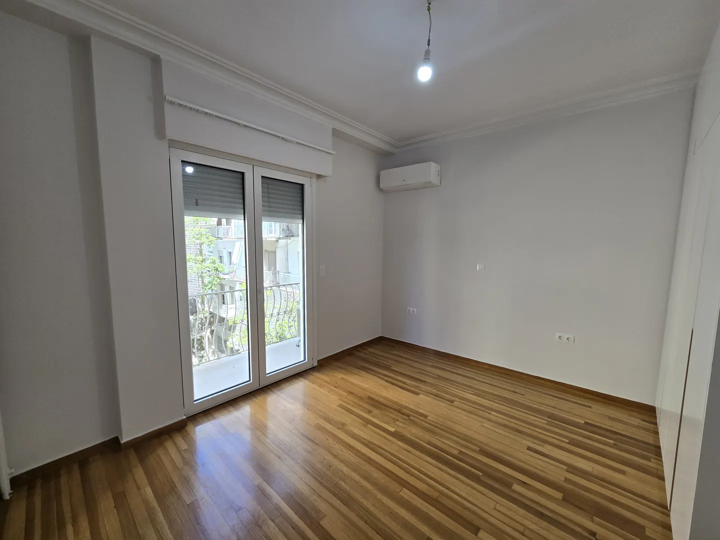 Bright, empty room with hardwood floors, white walls, and a sliding glass door to a balcony.