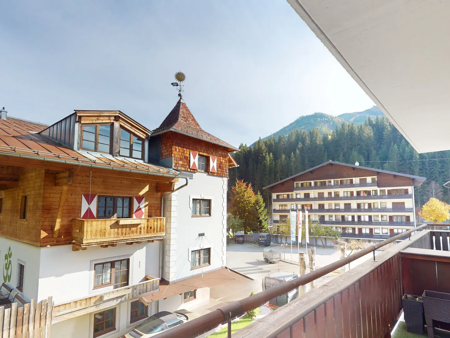 View from a balcony of a chalet-style building with wood and white facade, red and white shutters, and a mountain backdrop.