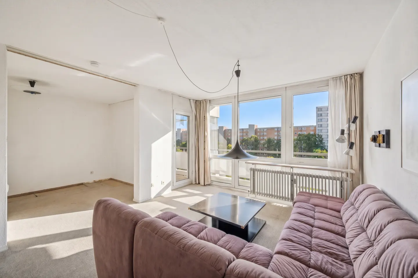 Bright living room with a mauve sectional sofa, black coffee table, and large windows overlooking a city view.
