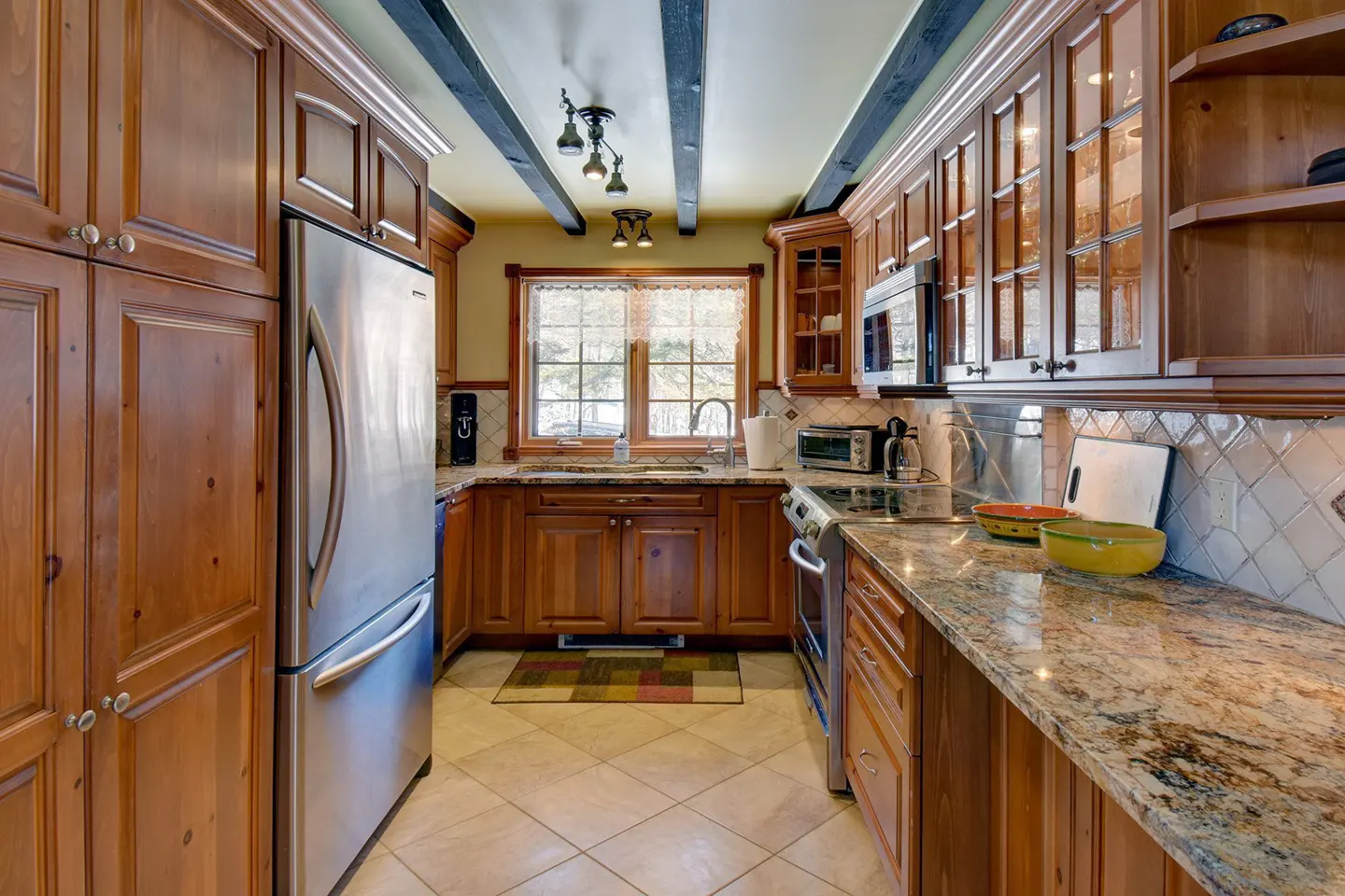 A kitchen with wood cabinets, stainless steel appliances, and granite countertops. Black beams accent the ceiling.
