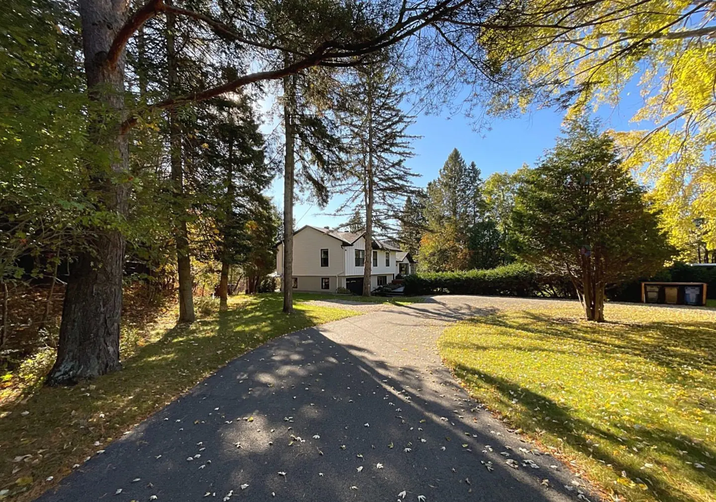 A long driveway leads to a two-story house surrounded by trees and green grass.