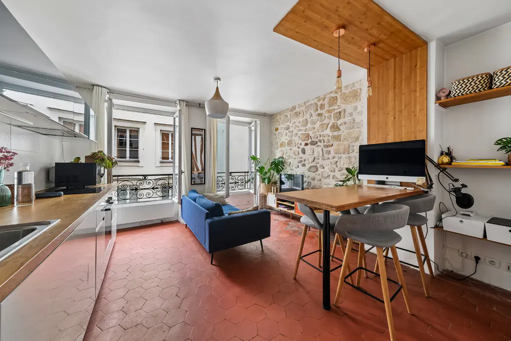 Modern studio apartment with red hexagonal tile floors, a blue sofa, and a wooden breakfast bar with grey stools.