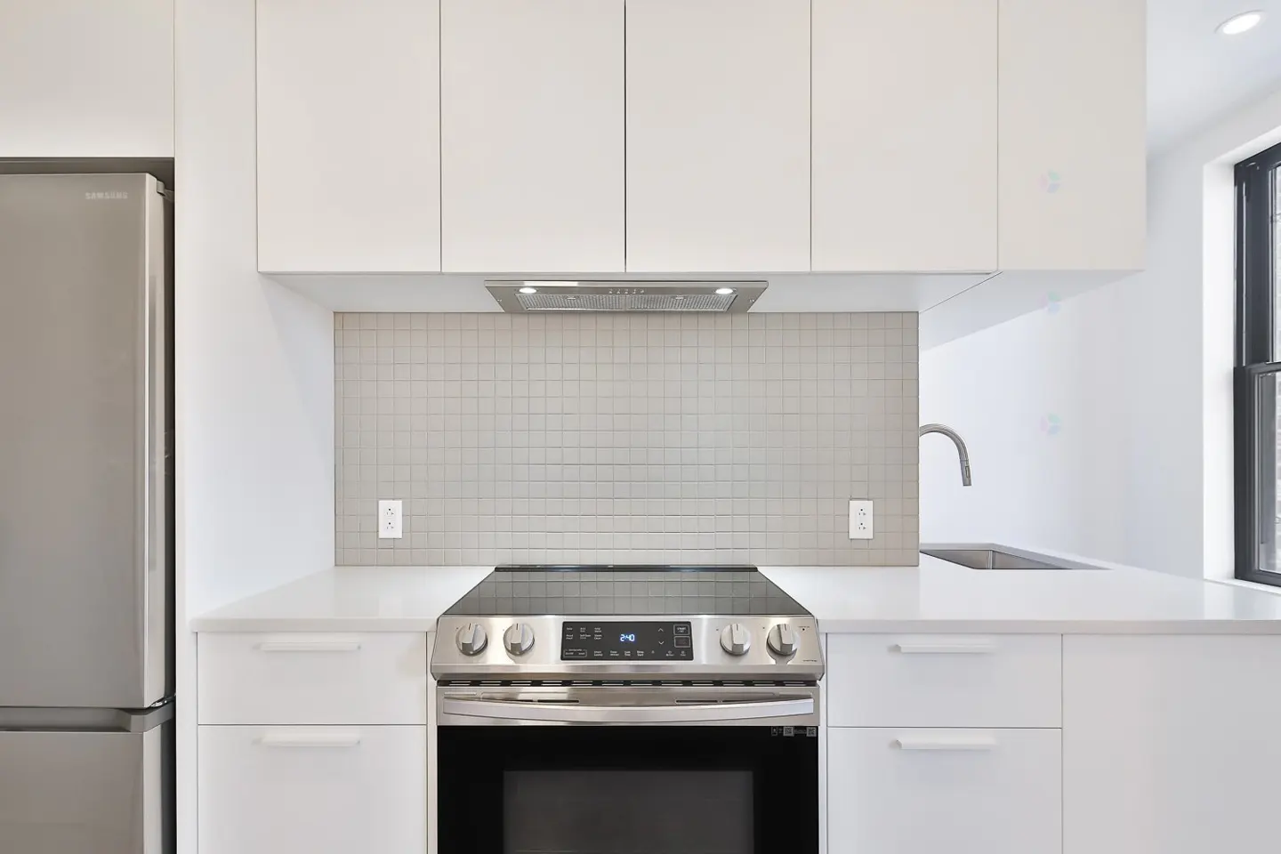 A modern kitchen with white cabinets, stainless steel appliances, and a light gray tiled backsplash.