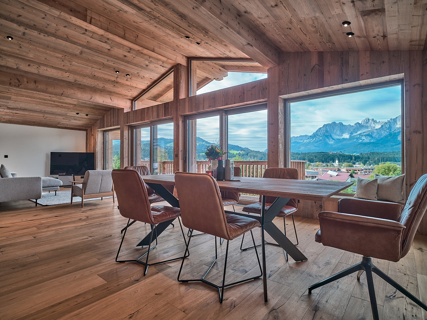 Modern dining room with wood walls and ceiling, leather chairs, and large windows overlooking a scenic mountain landscape. [AI-generated text]