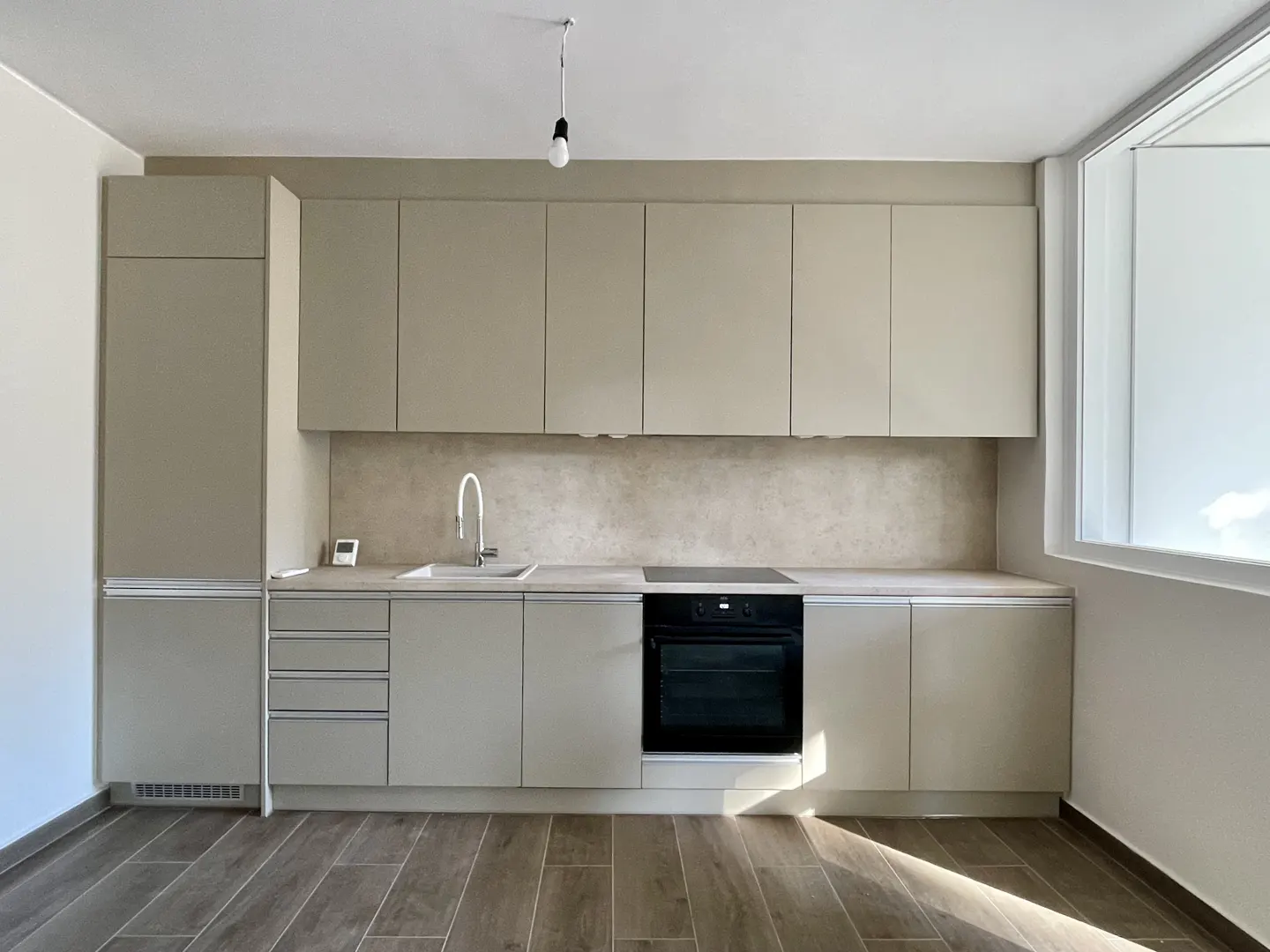 Bright kitchen with light gray cabinets, black oven, sink, and wood-look tile floor. A window provides natural light.