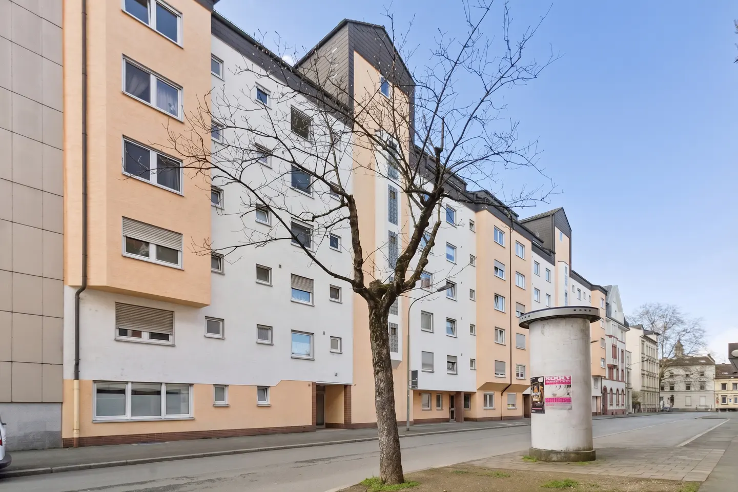 Exterior view of a multi-story apartment building with peach and white facade, windows, and a bare tree in front.