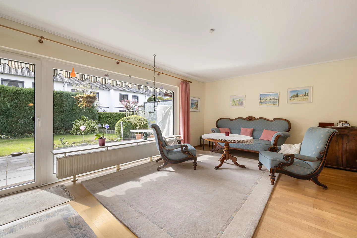 Living room with blue antique furniture, a round table, and a large window overlooking a green garden.