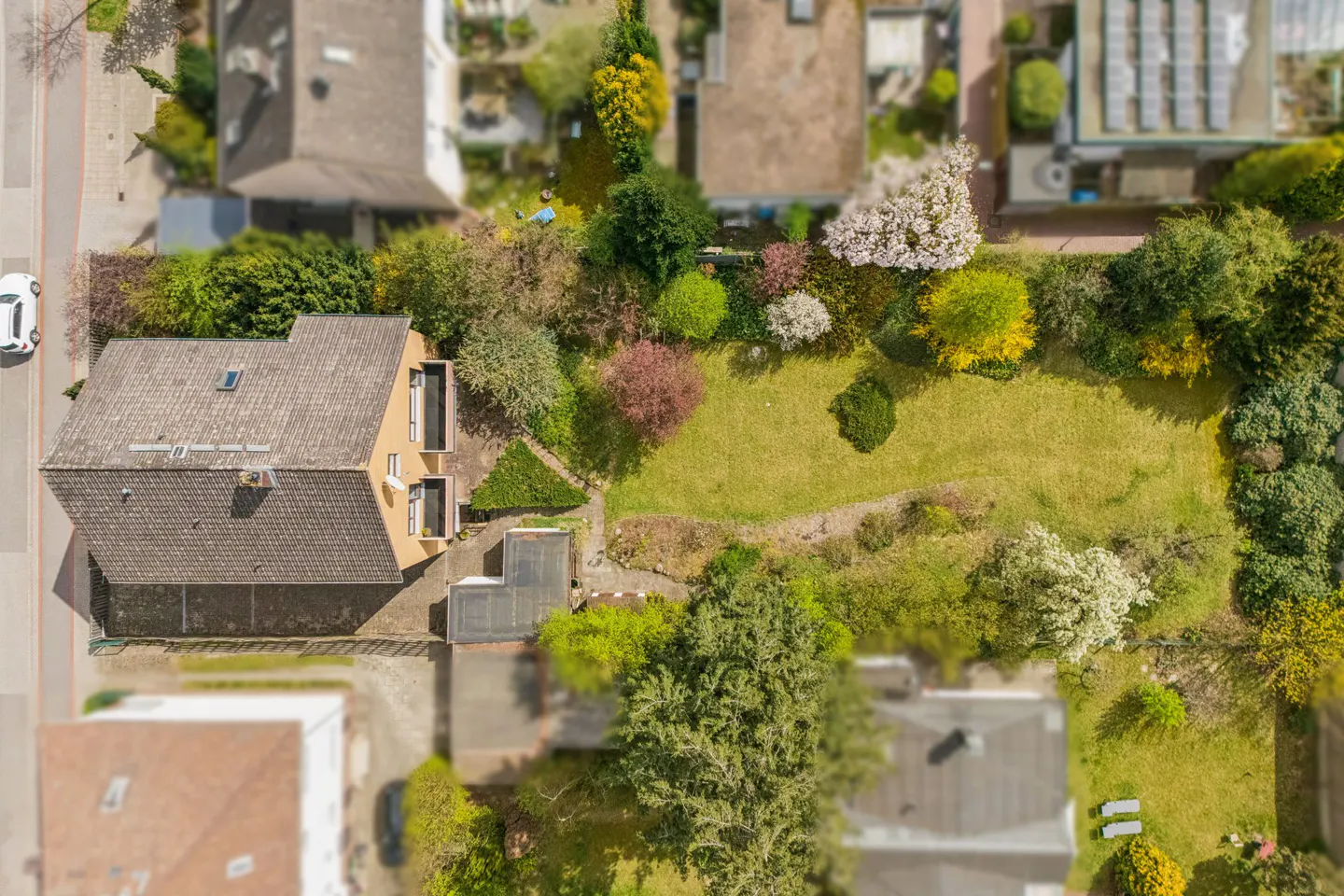 Aerial view of a tan house with a brown roof and a large green lawn with trees and bushes.