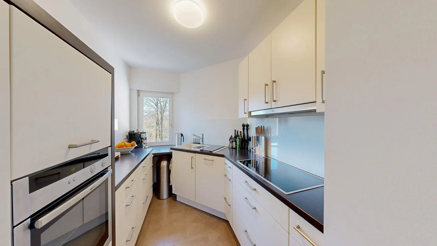 A bright kitchen with white cabinets, dark countertops, and stainless steel appliances. A window provides natural light.