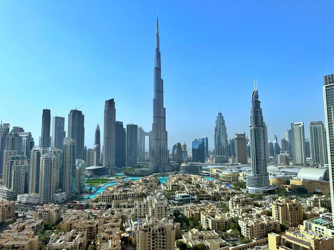 Dubai skyline view with Burj Khalifa towering over buildings and blue sky. Low-rise buildings in foreground.