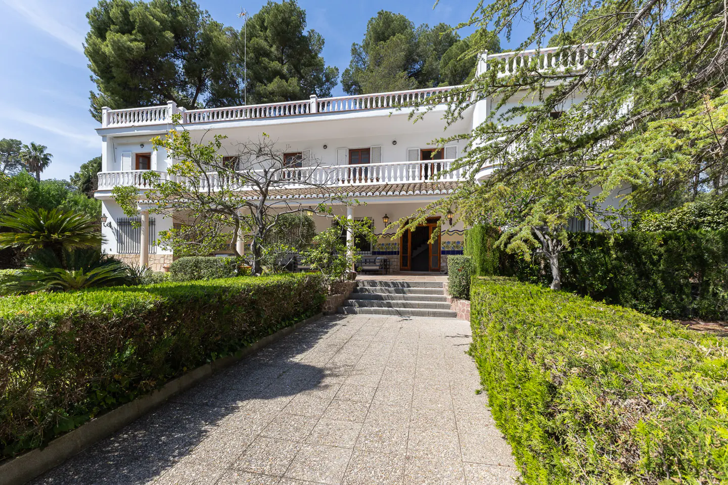 Two-story white house with a stone walkway leading to the front door, surrounded by green hedges and trees.