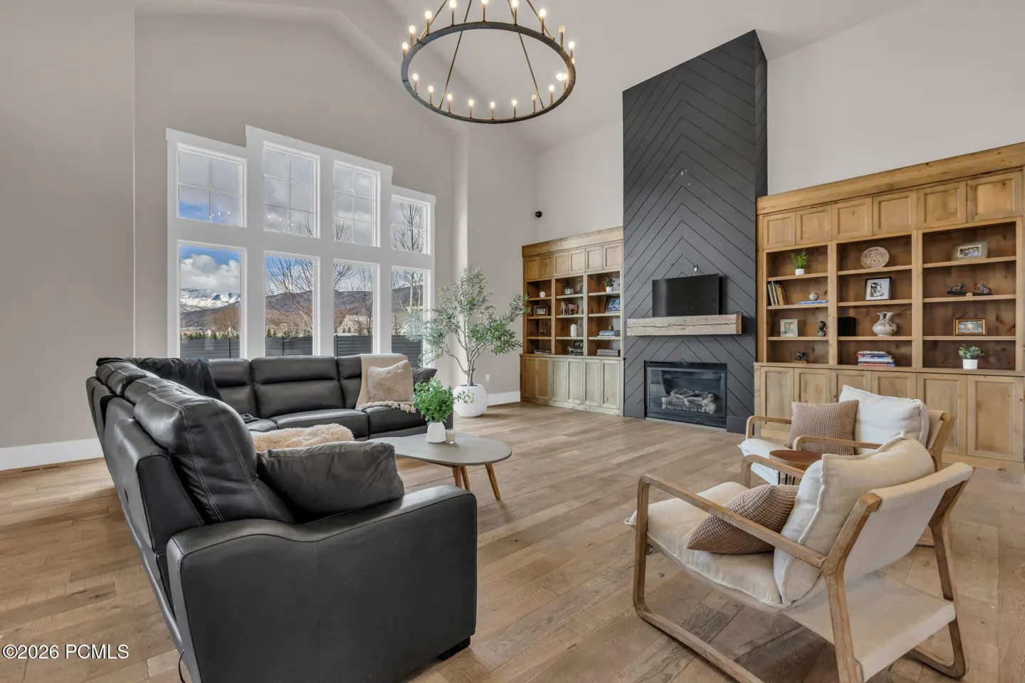 Bright living room with a black leather couch, wood floors, and a fireplace with built-in shelves. Large windows show a mountain view.