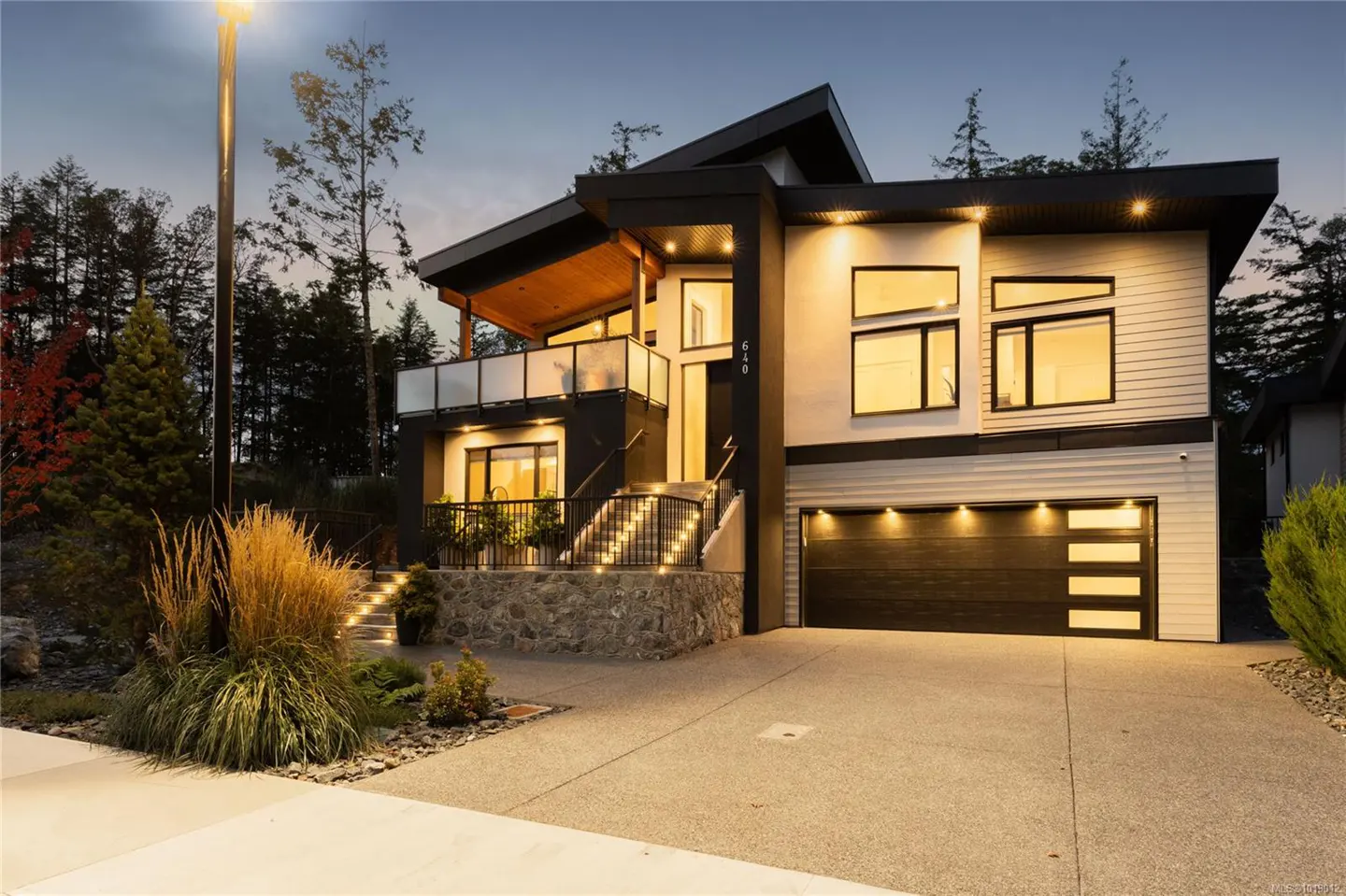 A modern two-story house with a black garage door, white siding, and a balcony at dusk.