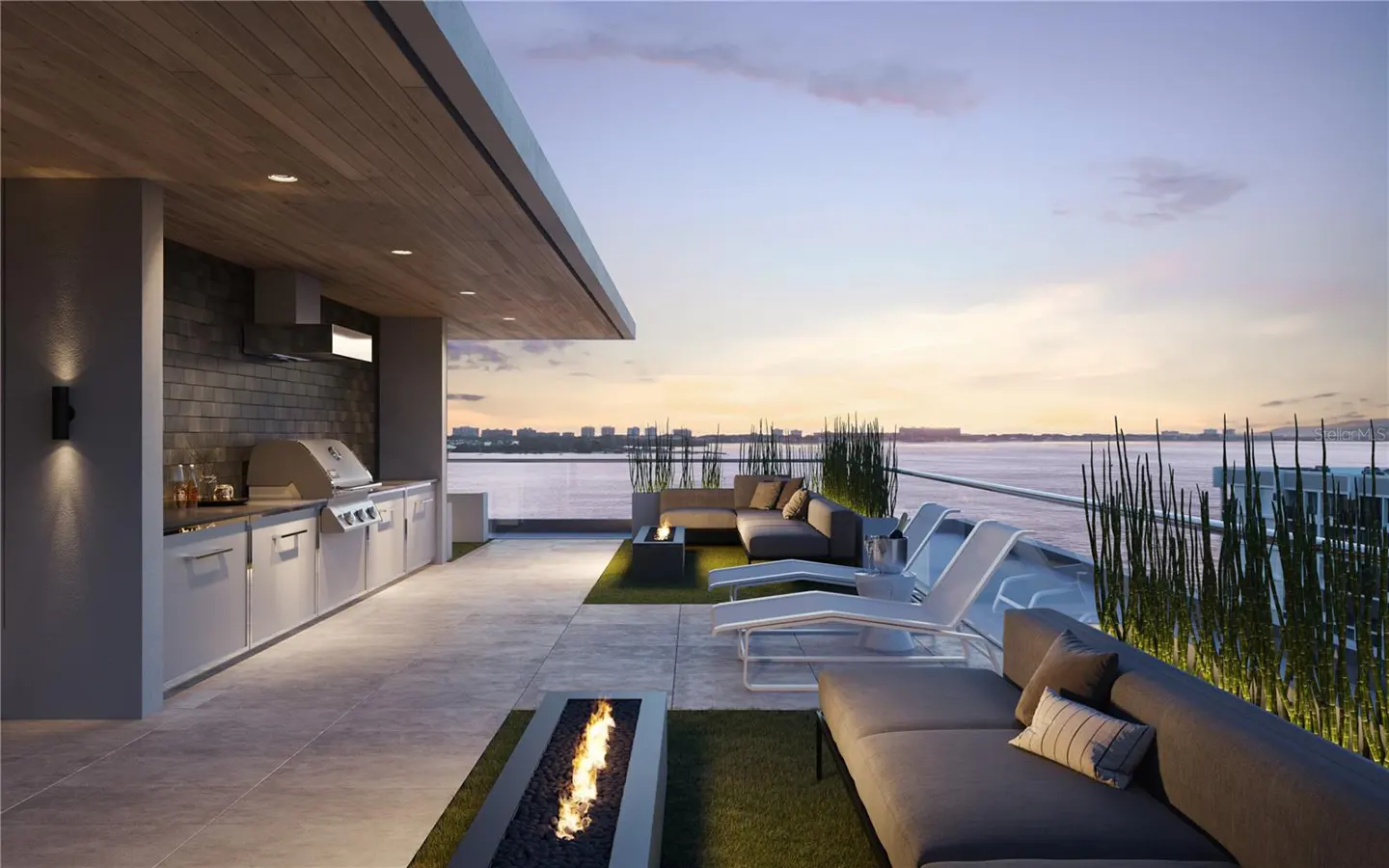 Rooftop patio with outdoor kitchen, grill, and seating area. Fire pits, lounge chairs, and a view of the water at sunset.