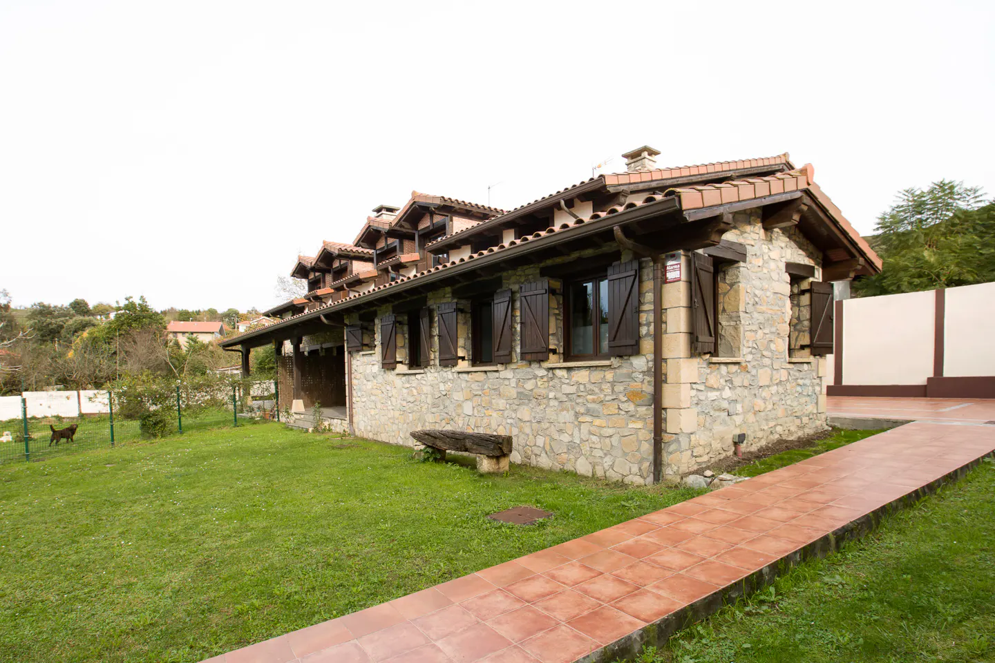 Stone house with brown shutters and a red tile roof. A red tile path leads to the house, and a green lawn surrounds it.