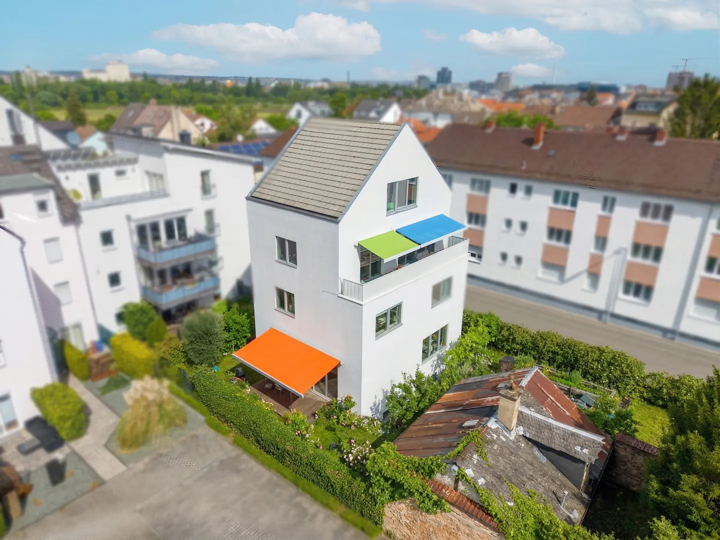 Aerial view of a modern, white, three-story house with colorful awnings in an urban setting.