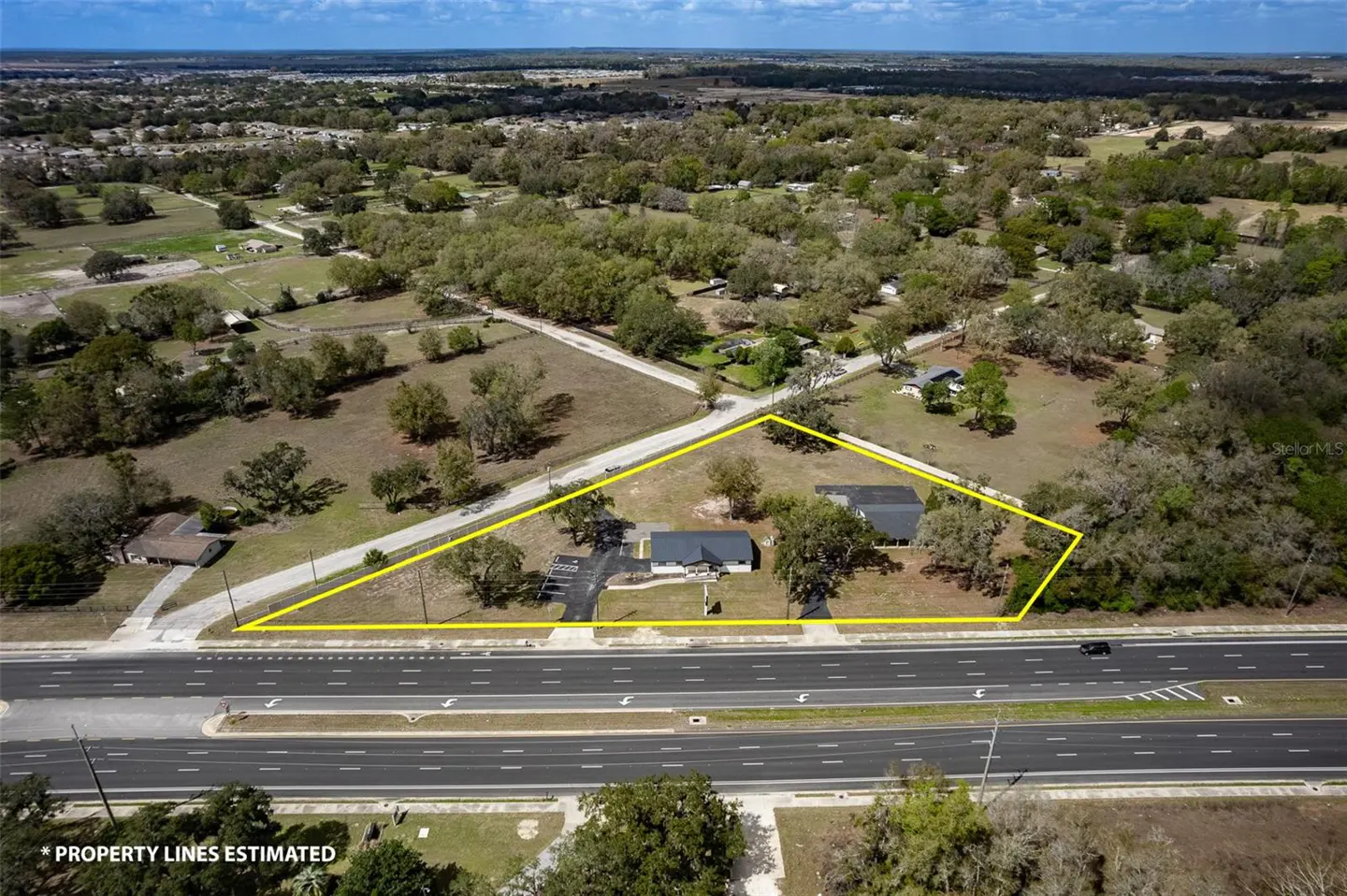 Aerial view of a property with two buildings outlined in yellow, next to a highway and surrounded by trees.