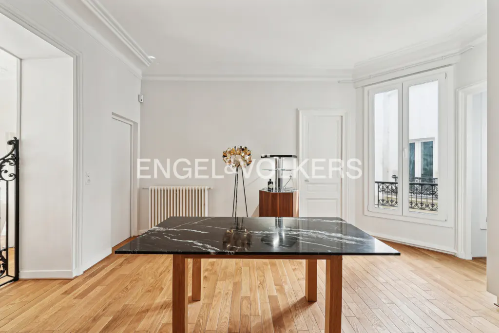 Bright room with wood floors, white walls, and a black marble table. A window with a balcony is on the right.