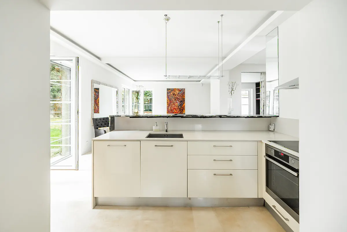 Bright, modern kitchen with white cabinets, black sink, and stainless steel oven. Open floor plan with art and garden view.