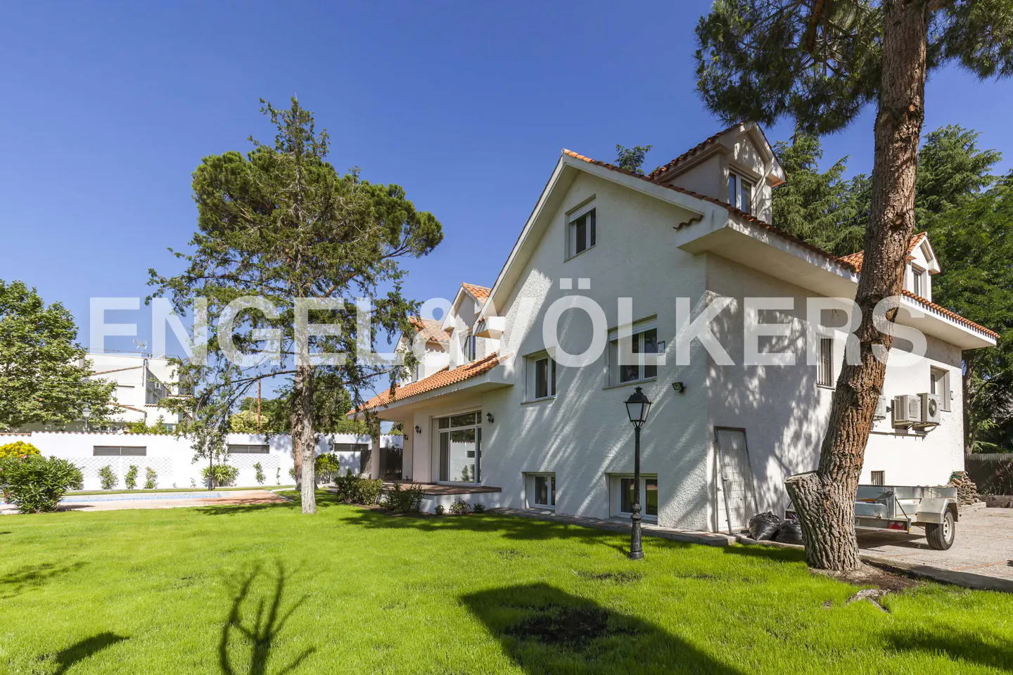 Exterior view of a white two-story house with an orange roof, green lawn, trees, and a trailer parked nearby.