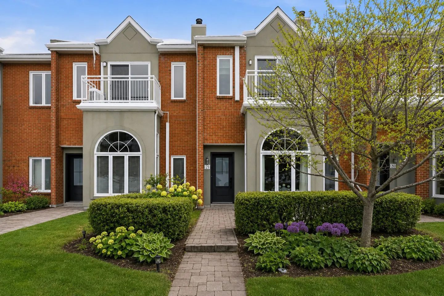 Exterior of a red brick townhouse with a black door, arched windows, and a small balcony. A stone path leads to the entrance.