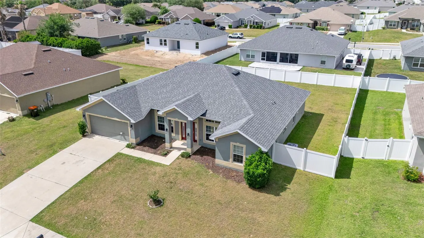 Aerial view of a single-story gray house with a gray roof, a driveway, and a white fence enclosing the backyard.