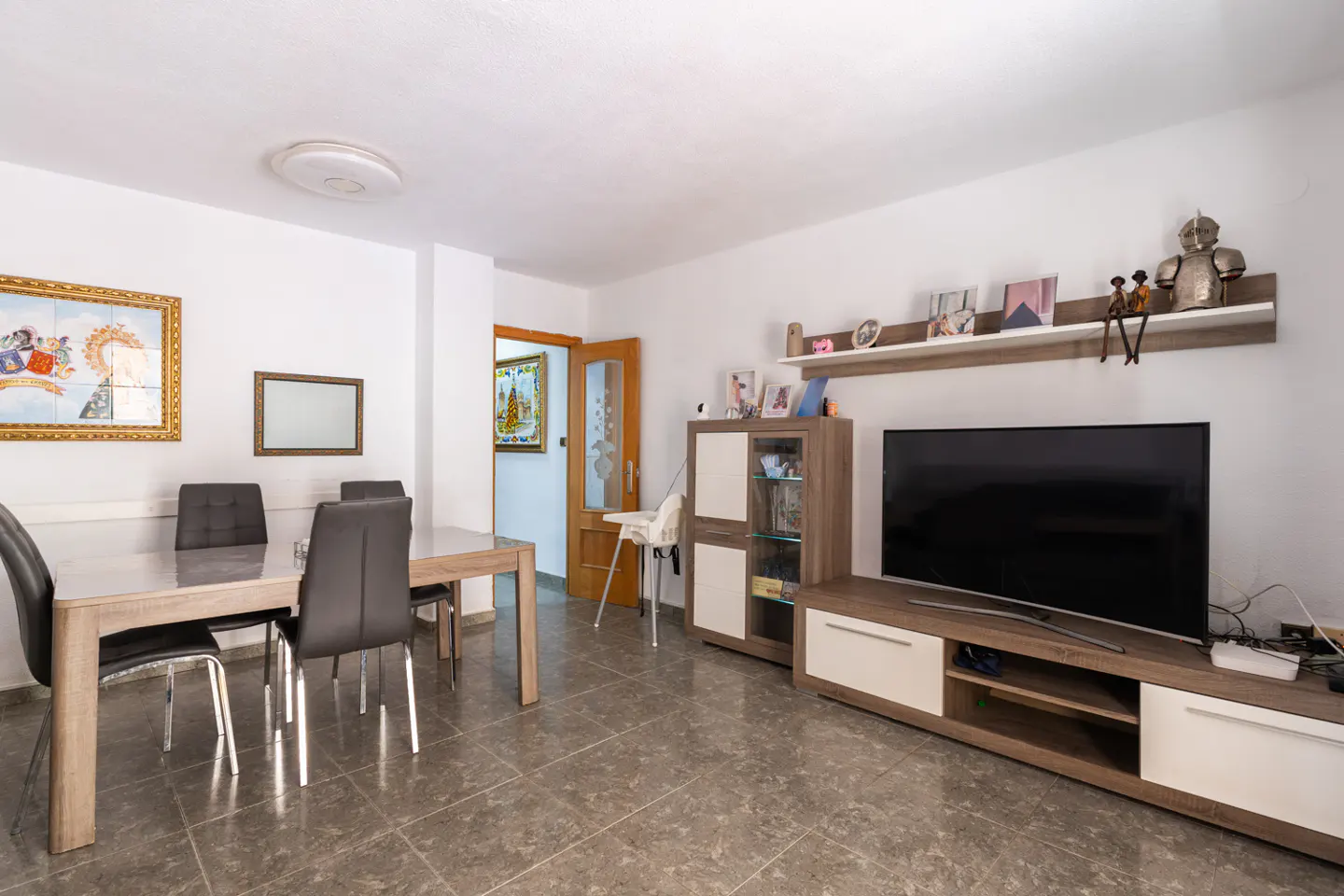 A living room with a dining table, chairs, TV, and cabinet on a tiled floor.