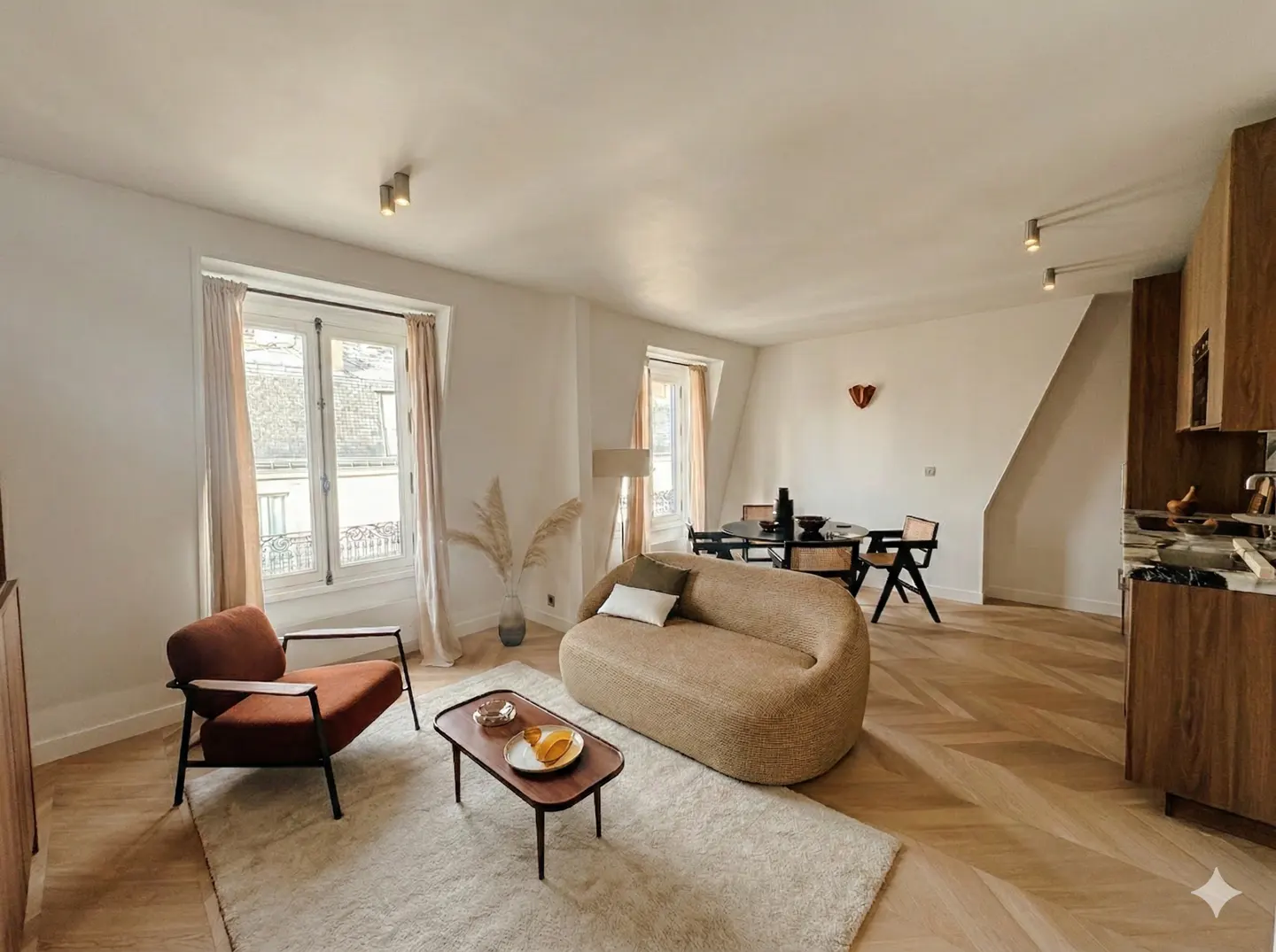 Modern open-plan living room with a beige curved sofa, rust-colored armchair, wooden coffee table, and herringbone floors.