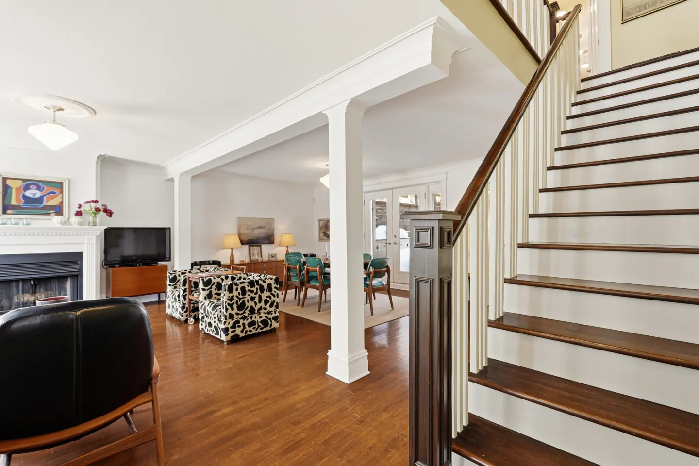 Open-concept living room with hardwood floors, white walls, and a staircase with white risers and a dark wood banister.