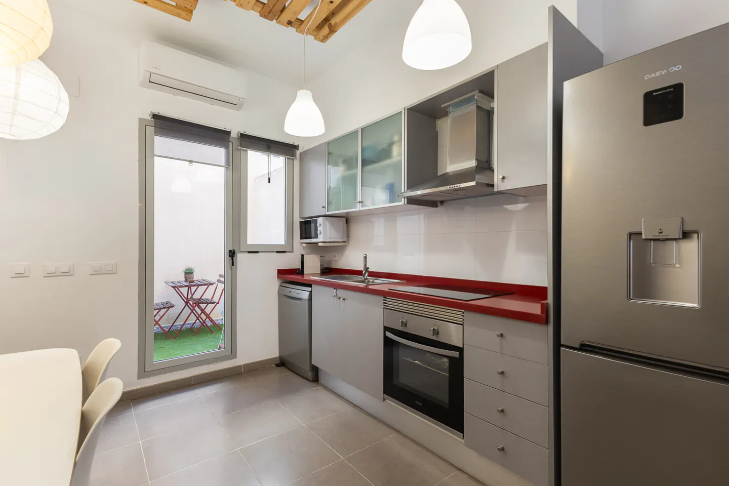 Modern kitchen with grey cabinets, red countertops, stainless steel appliances, and a door leading to a small patio.