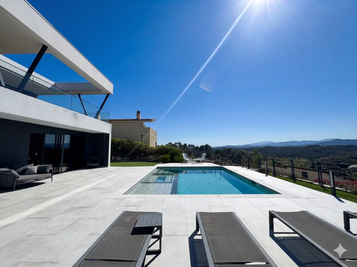Modern white house with a pool, lounge chairs, and a view of distant mountains under a bright blue sky.