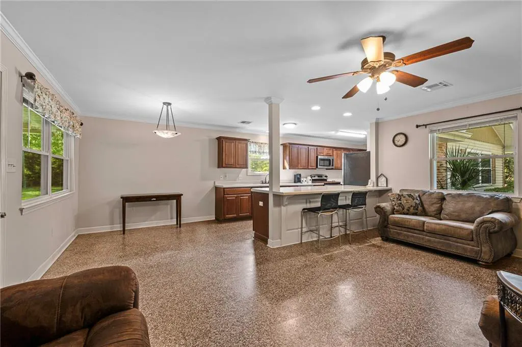 Open-concept living space with brown speckled floors, a kitchen with dark wood cabinets, and a brown leather sofa.