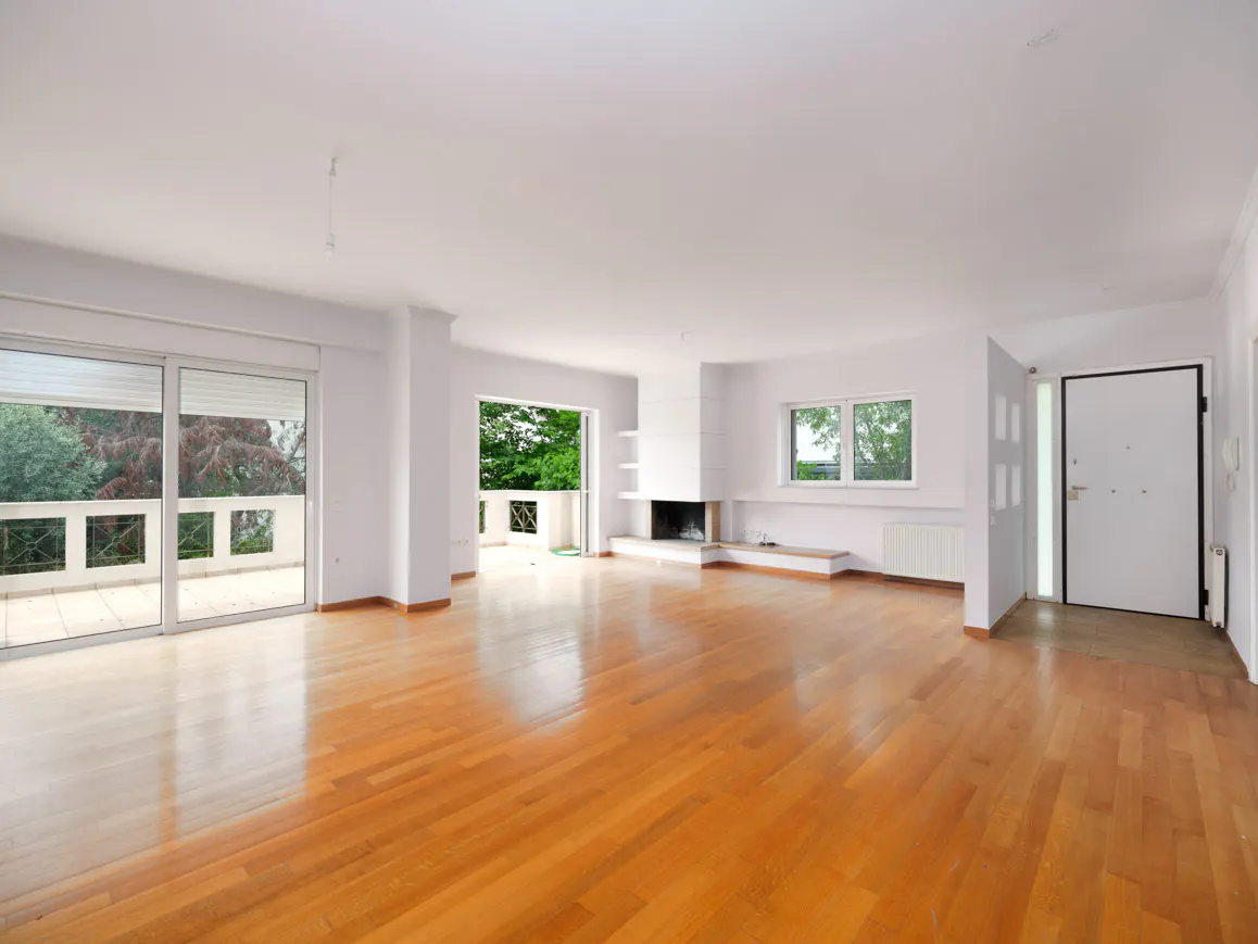 Bright, empty living room with hardwood floors, white walls, fireplace, and balcony access. A white door is visible on the right.