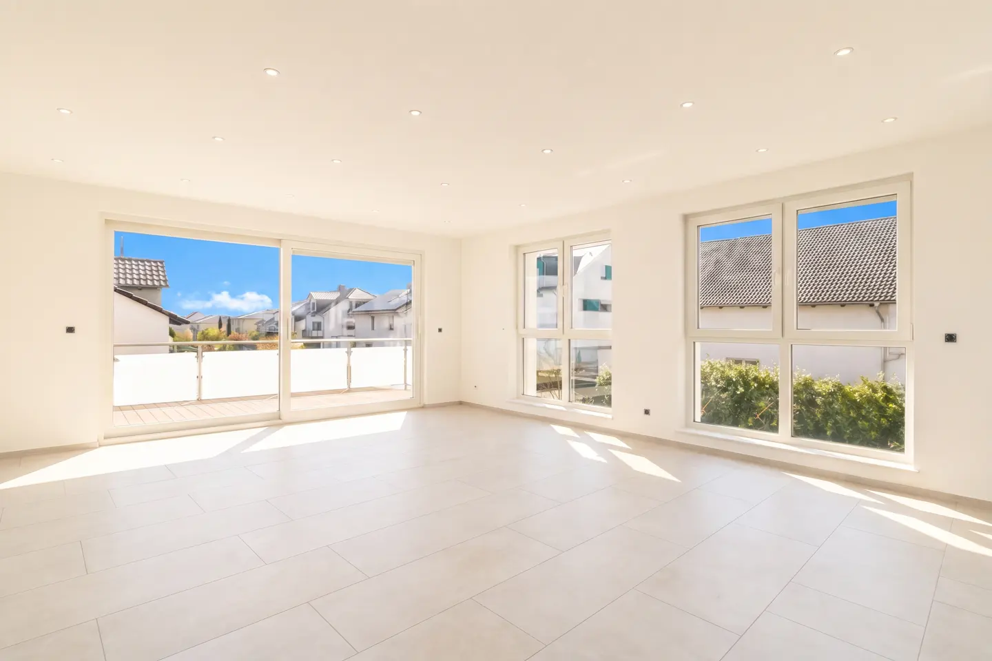 Bright, empty room with white walls, tile floor, and recessed lighting. Large sliding glass doors lead to a balcony with neighborhood views.
