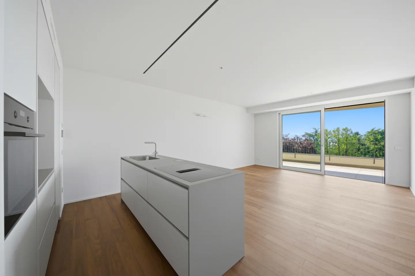 Bright, modern kitchen with white cabinets, island, and wood floors. Sliding glass doors open to a balcony with trees in the background.