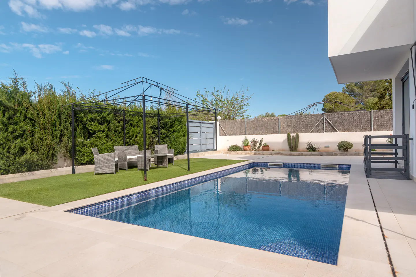 A backyard with a blue tiled pool, a black metal gazebo, and a gray wicker patio set.