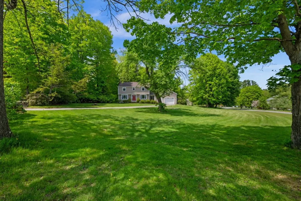 Two-story gray house with red door, surrounded by green trees and a large green lawn.