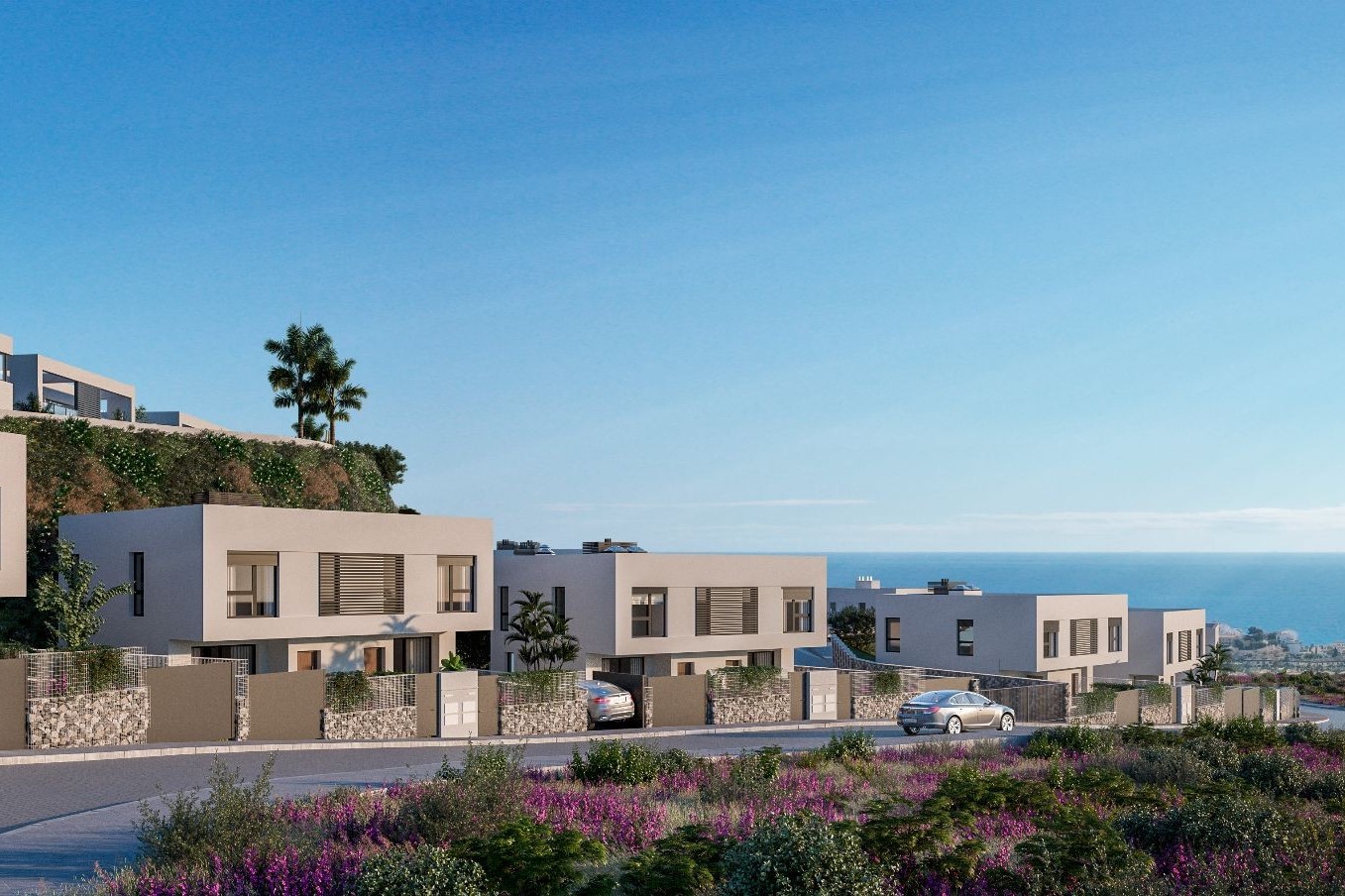 Modern, beige townhouses line a street with purple flowers. Cars are parked in driveways. The ocean and blue sky are in the background.