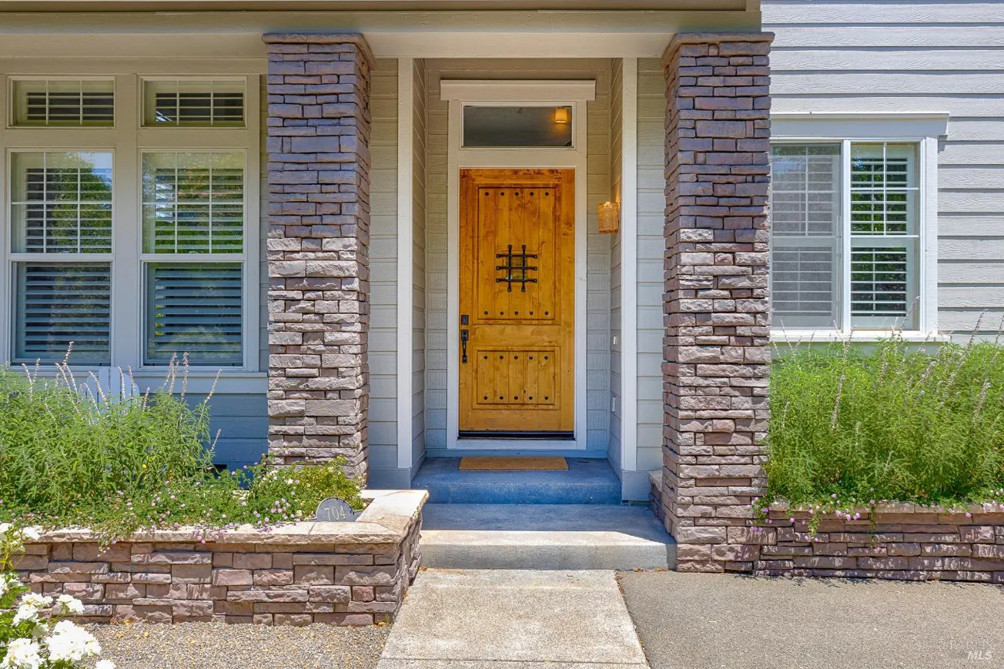 Home exterior featuring a wooden front door with iron detail, flanked by stone pillars and windows with white trim.