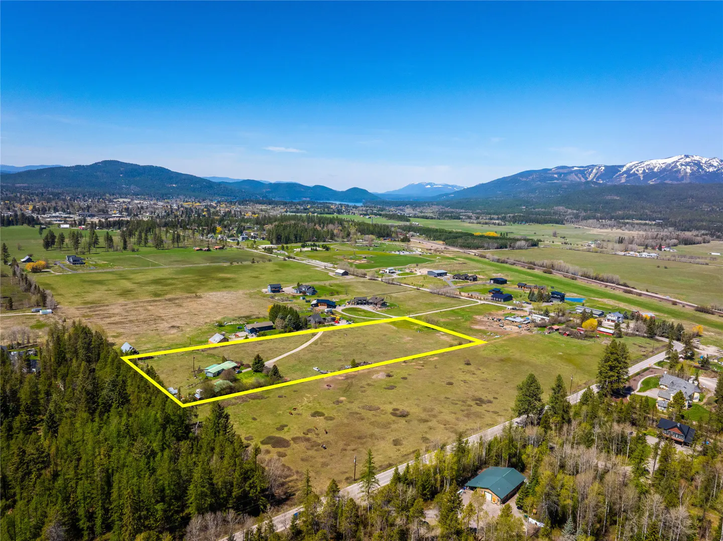Aerial view of a large grassy lot outlined in yellow, with mountains and trees in the background.