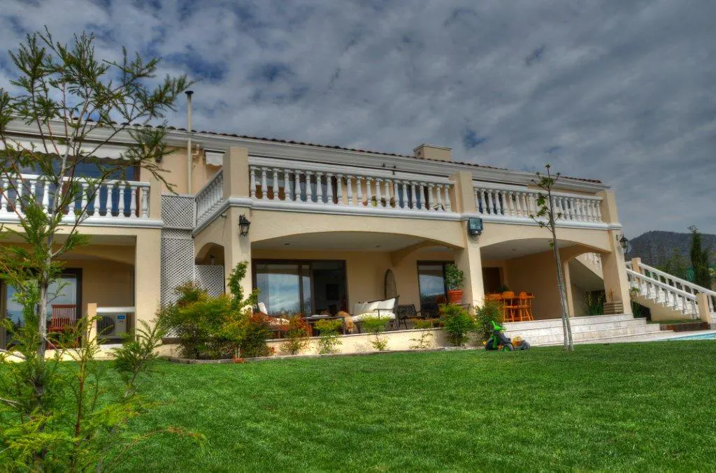 Two-story beige house with white balconies, a green lawn, and cloudy sky.