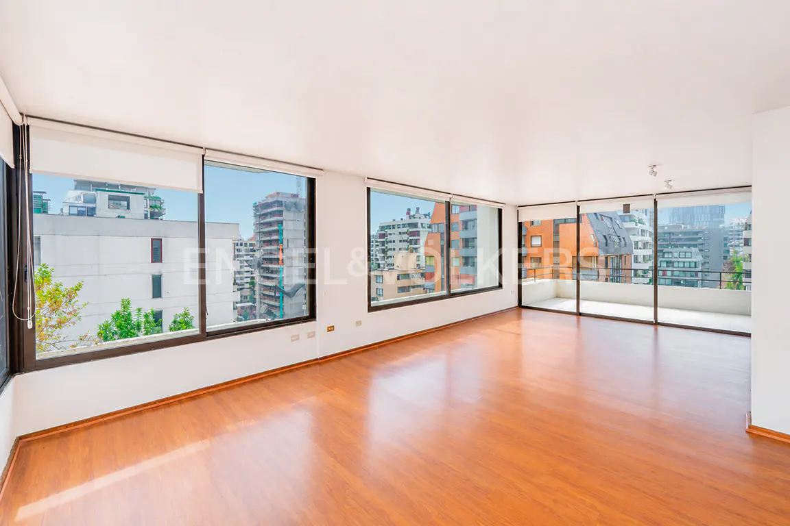 Empty living room with polished wood floors, white walls, and large windows overlooking a city skyline.