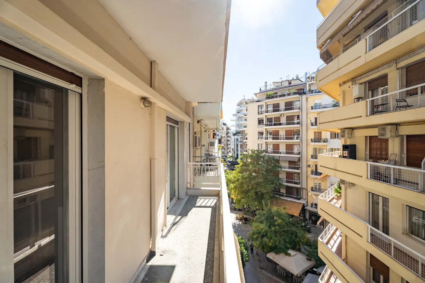 View from a balcony with beige walls and white railings, overlooking a city street with apartment buildings.