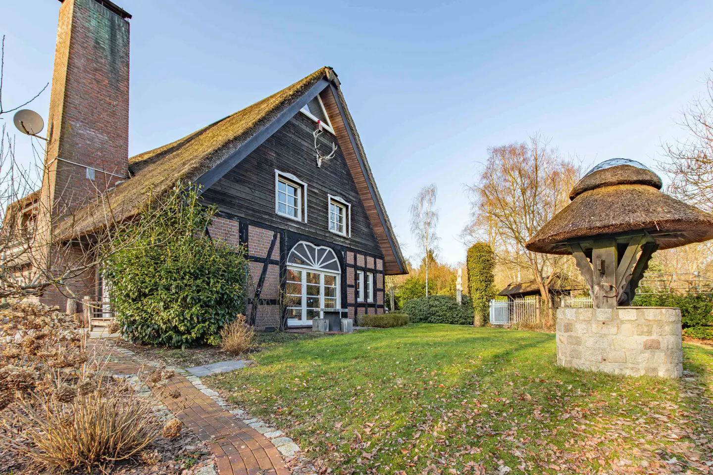 Exterior view of a black and brick house with a thatched roof and a well in the yard.